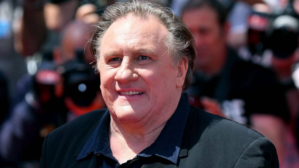 Portrait of Gérard Depardieu smiling warmly with blurred press background bright lighting Wallpaper