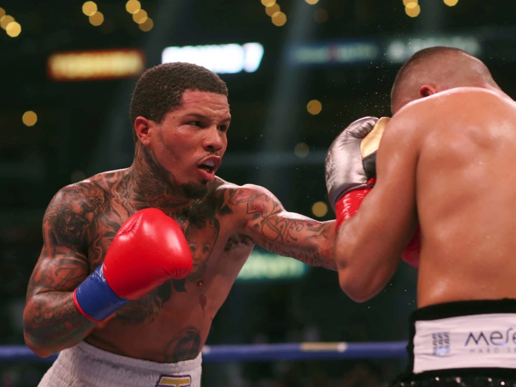 Gervonta Davis boxing action with red gloves and tattoos in blurred arena background wallpaper