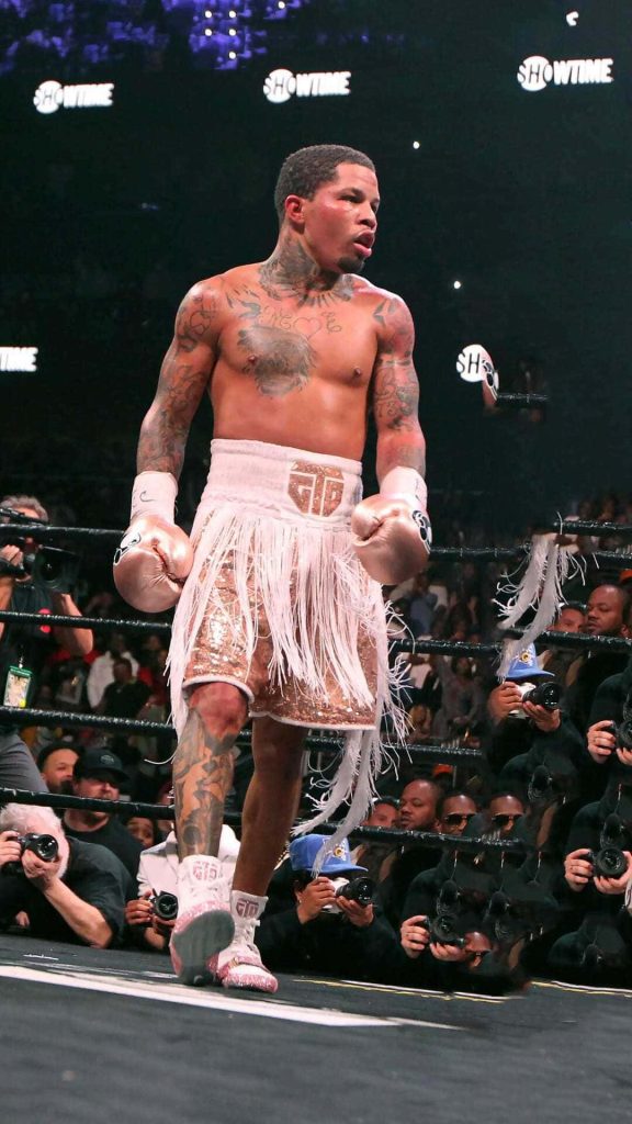 Gervonta Tank Davis in white gold boxing trunks fights fiercely under arena lights with photographers Wallpaper