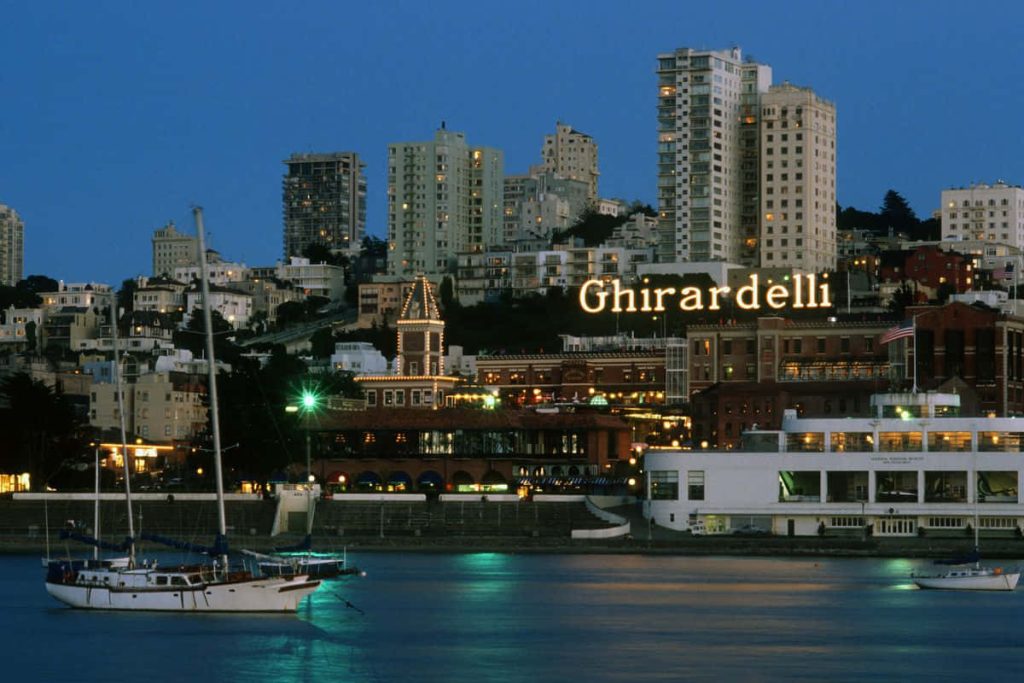 Ghirardelli Square illuminated sign at twilight over San Francisco waterfront with sailboats Wallpaper