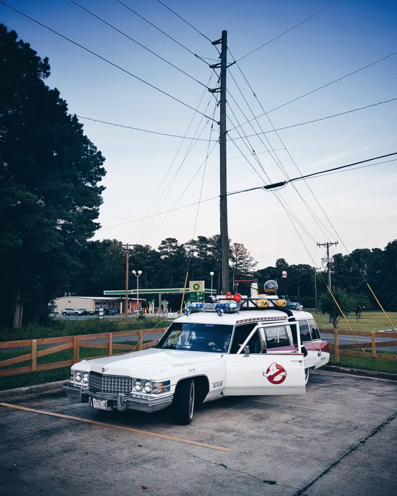 Ghostbusters Ecto-1 parked at twilight with door open in suburban lot cinematic wallpaper