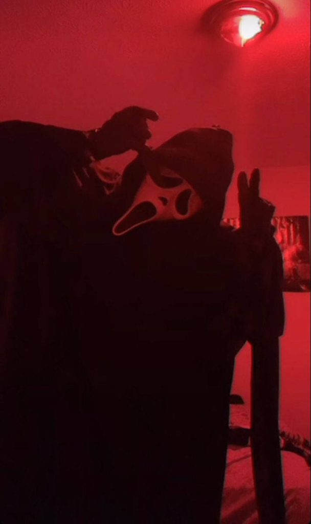 Ghostface from Scream making a peace sign in red-lit dark room horror wallpaper background