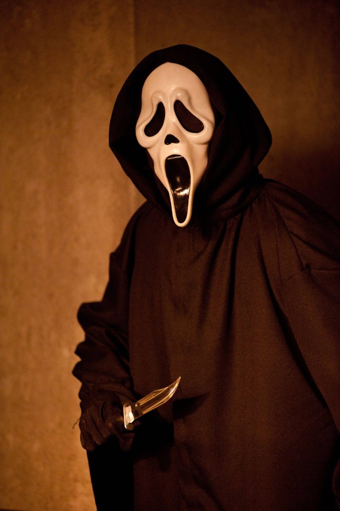 Ghostface from Scream horror film in black hooded robe holding knife with moody lighting Wallpaper