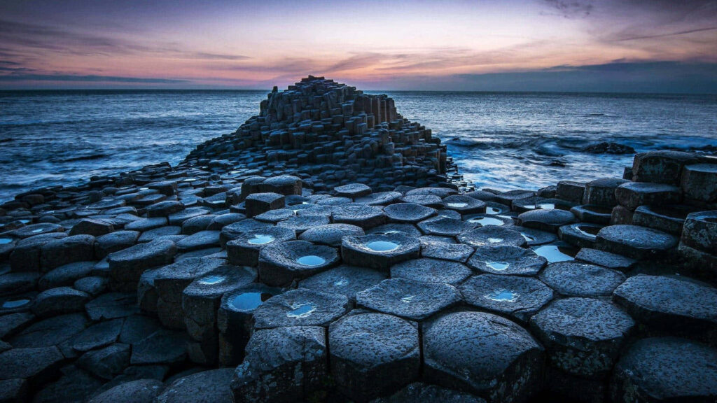 Giant's Causeway: Majestic Rock Piles Amidst a Serene Ocean Backdrop at Sunset Wallpaper