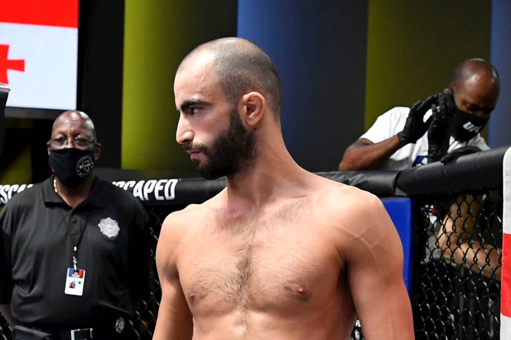 High-resolution wallpaper of UFC fighter Giga Chikadze shirtless in octagon cage with officials