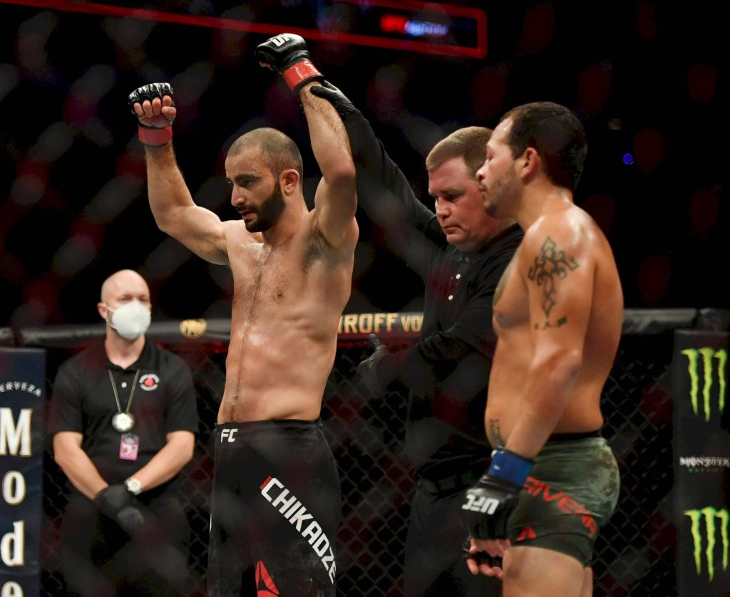 Giga Chikadze celebrates UFC victory with referee opponent Jimmie Rivera watches intense fight background Wallpaper