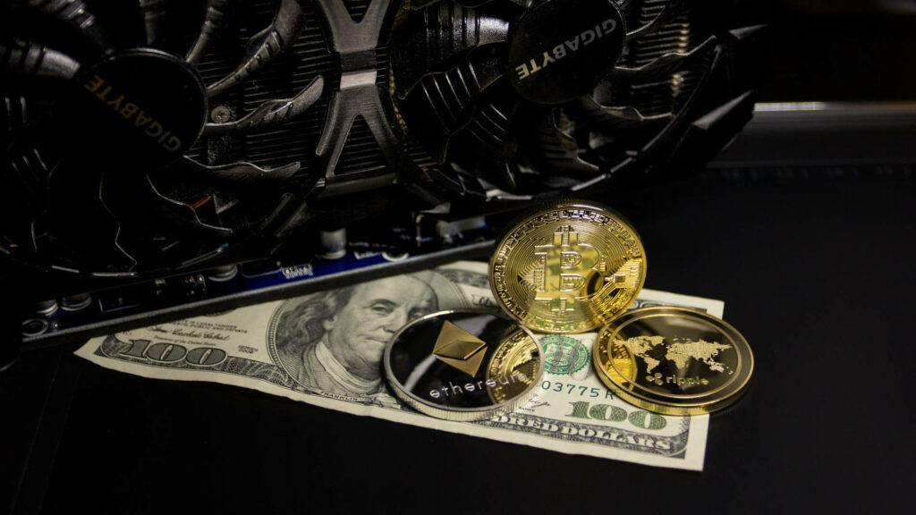 Close-up of Gigabyte graphics card with Ethereum Bitcoin Ripple coins on US hundred-dollar bill Wallpaper