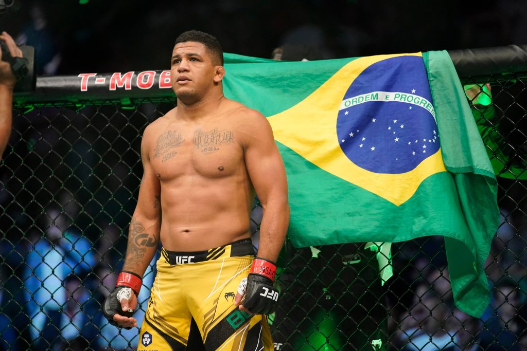 Gilbert Burns in UFC octagon with Brazilian flag focus yellow fight shorts intense arena Wallpaper