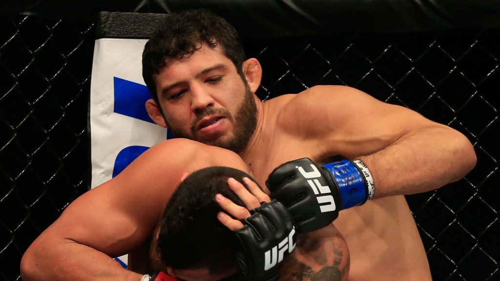 MMA fighter Gilbert Melendez clinches opponent in UFC cage with intense arena lighting background Wallpaper