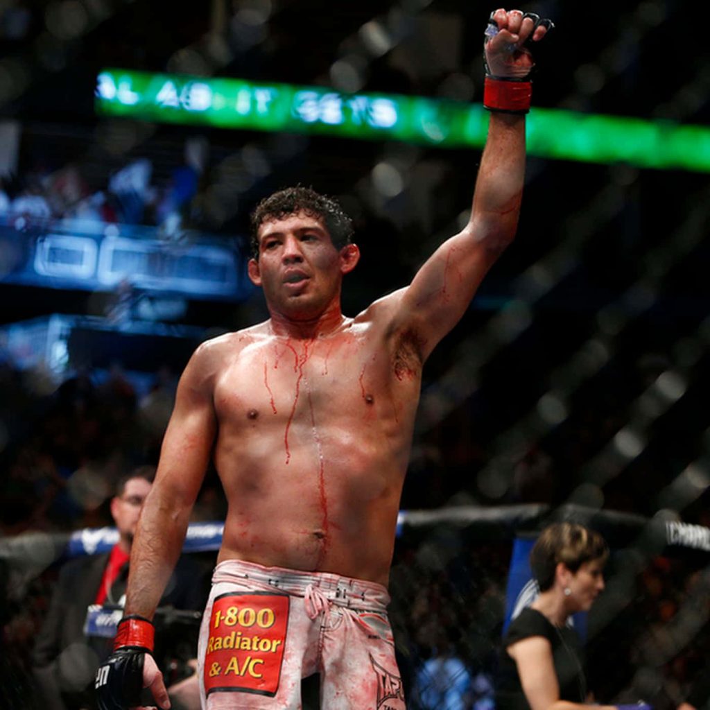 MMA fighter Gilbert Melendez celebrates bloody victory in cage under bright arena lights wallpaper
