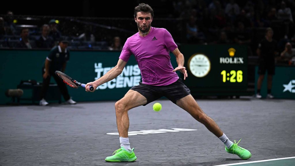 Gilles Simon lunging for forehand on indoor tennis court pink Adidas shirt Rolex clock background Wallpaper