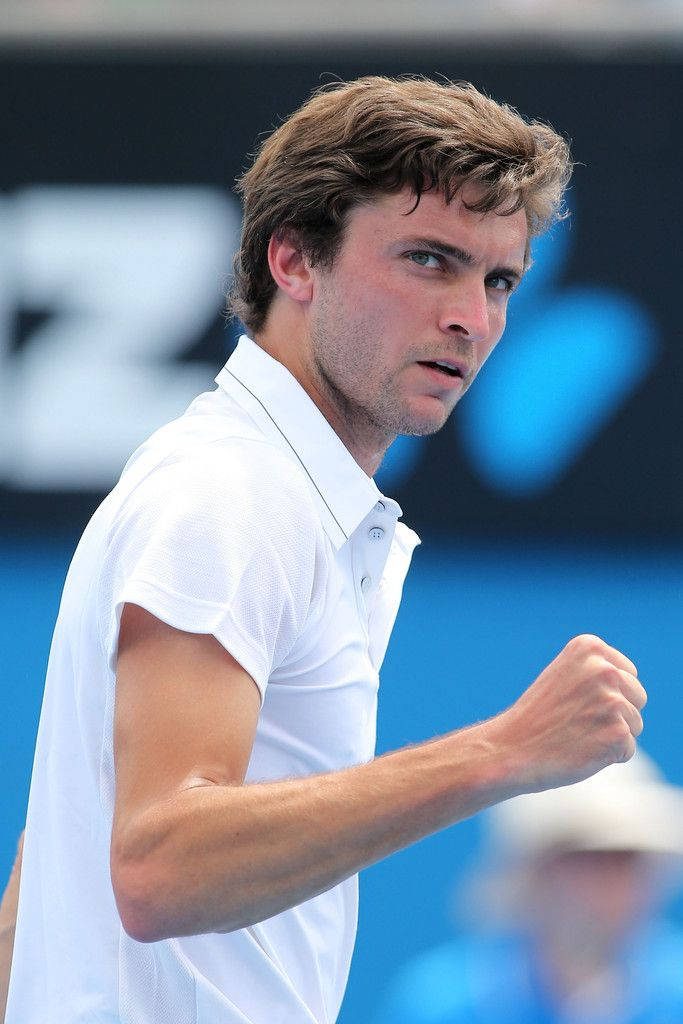 Professional tennis player Gilles Simon celebrating on vivid blue court sports wallpaper background