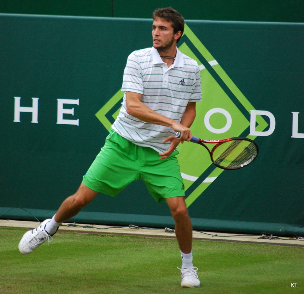 Gilles Simon in striped polo hitting tennis ball on grass court with Head racket dynamic action Wallpaper