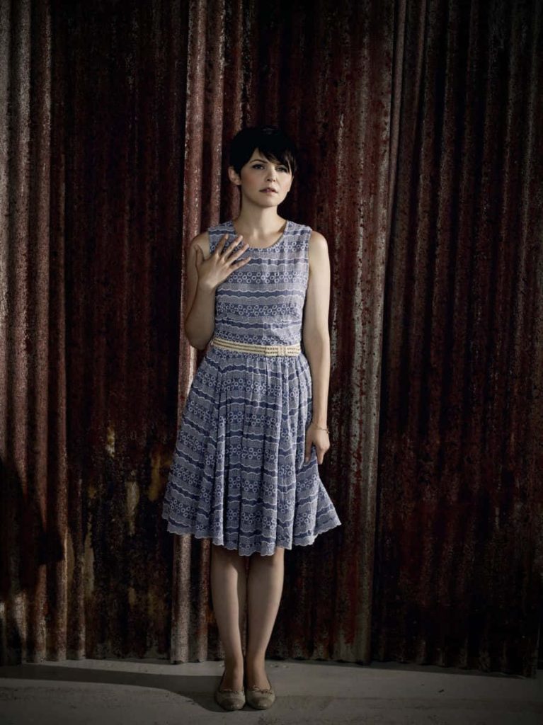 Ginnifer Goodwin in blue patterned midi dress with pixie cut against rustic metal wall wallpaper