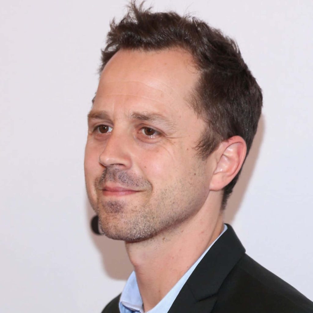 Professional headshot of actor Giovanni Ribisi smiling in dark blazer light shirt on white background Wallpaper