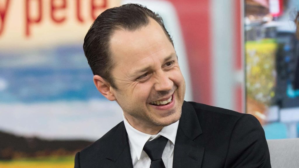 Giovanni Ribisi smiling in black suit in bright professional TV studio perfect wallpaper background