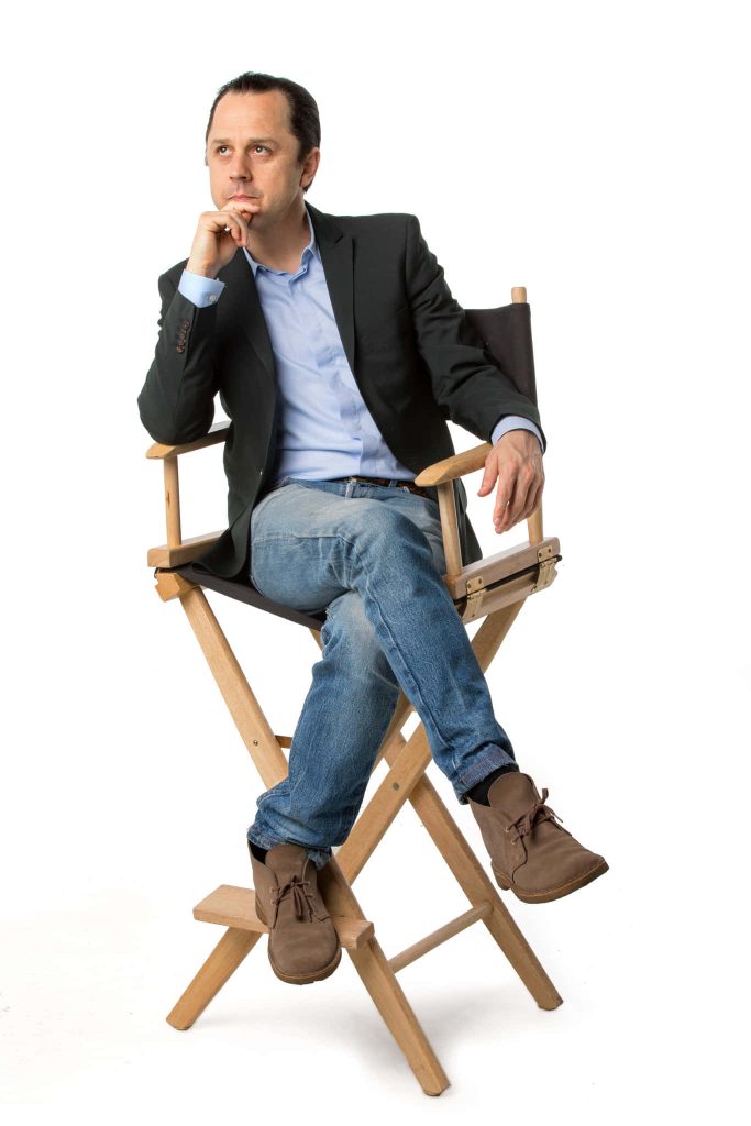 Actor Giovanni Ribisi in smart casual outfit sitting in director's chair against white background Wallpaper