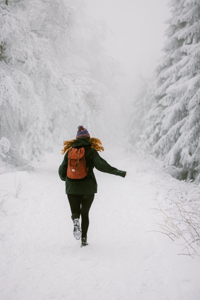 Girl with red backpack running through snowy winter forest fog serene nature landscape wallpaper