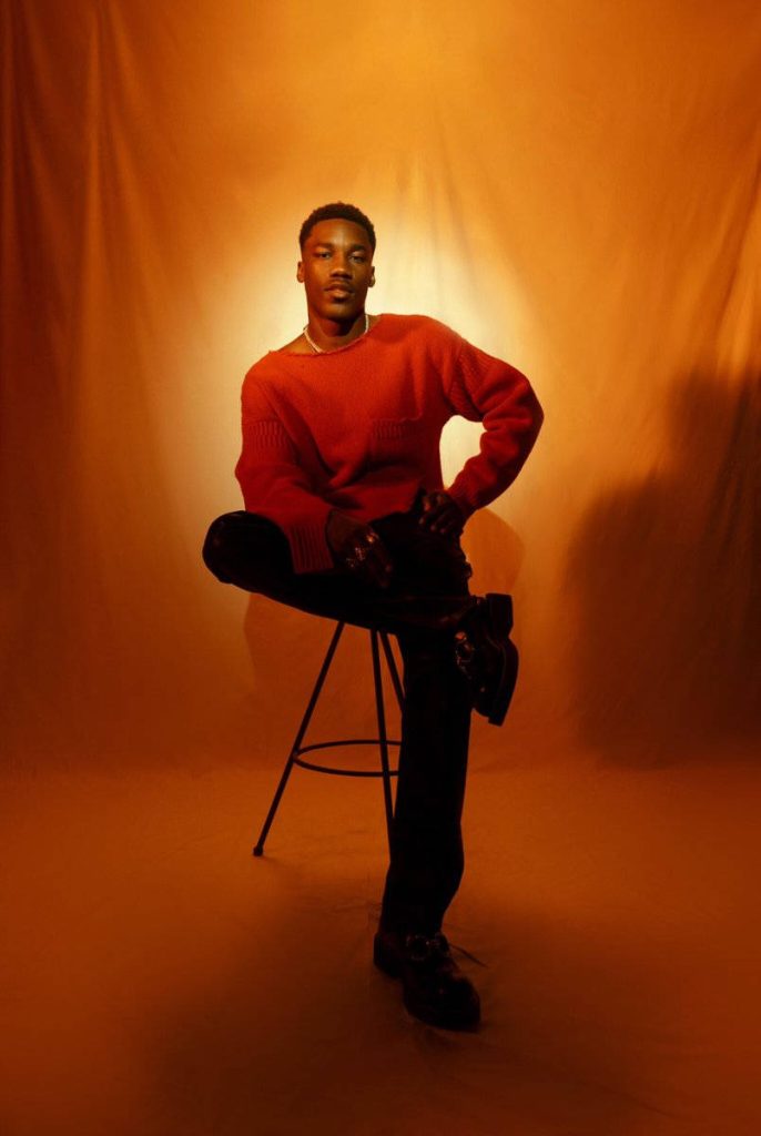 Giveon portrait in red sweater amber studio backdrop minimalist editorial R&B wallpaper background