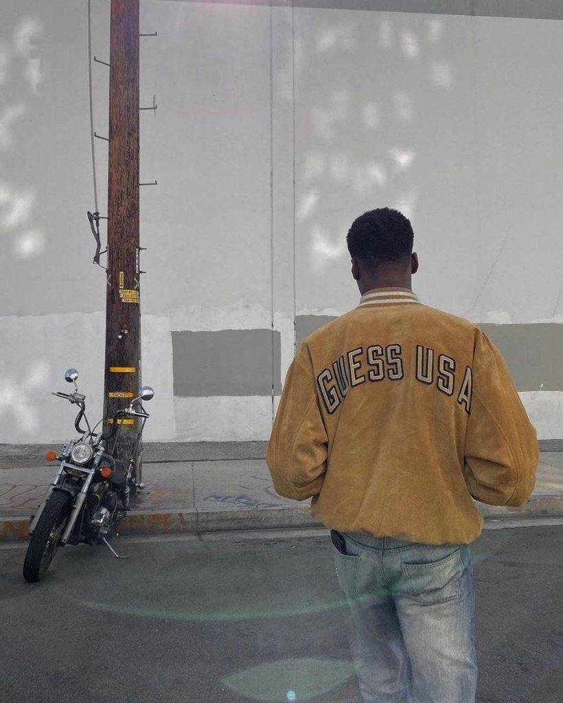 R&B artist Giveon in mustard GUESS varsity jacket by motorcycle urban street style wallpaper