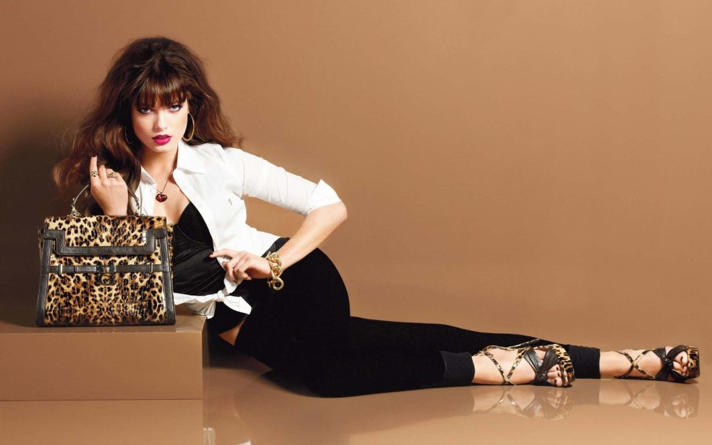 Brunette model in white shirt and black outfit posing with leopard print handbag on tan background Wallpaper