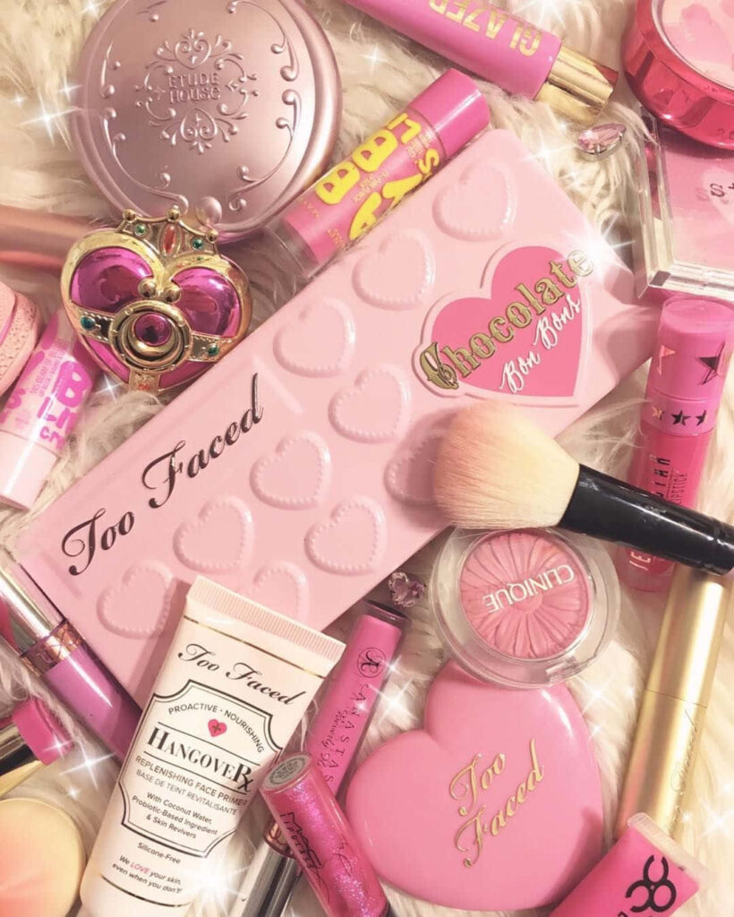 Too Faced and Clinique makeup flat lay with heart palettes lip glosses brushes pink sparkles Wallpaper