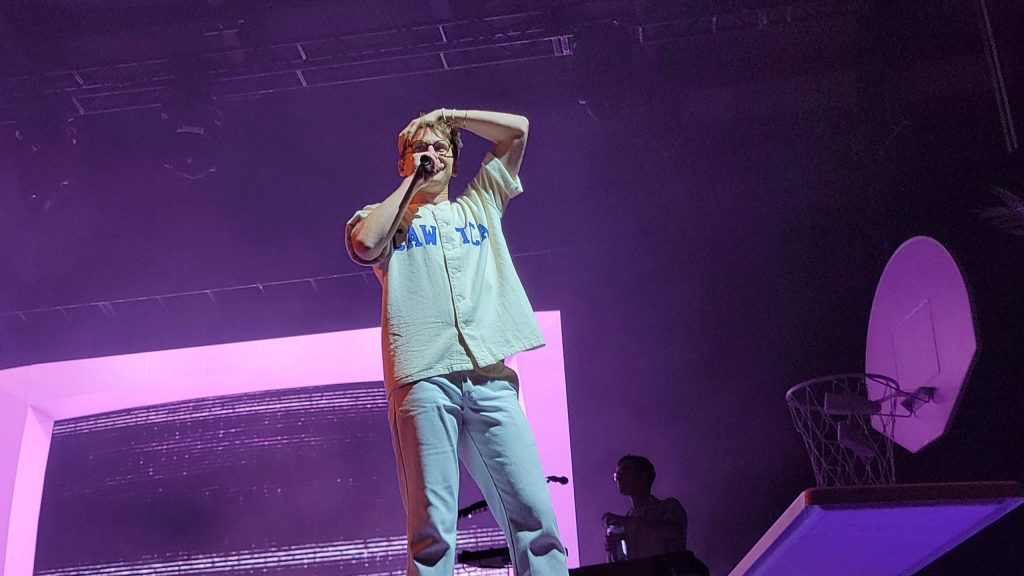 Glass Animals lead vocalist Dave Bayley performing live in iconic Lawn shirt under purple lights Wallpaper