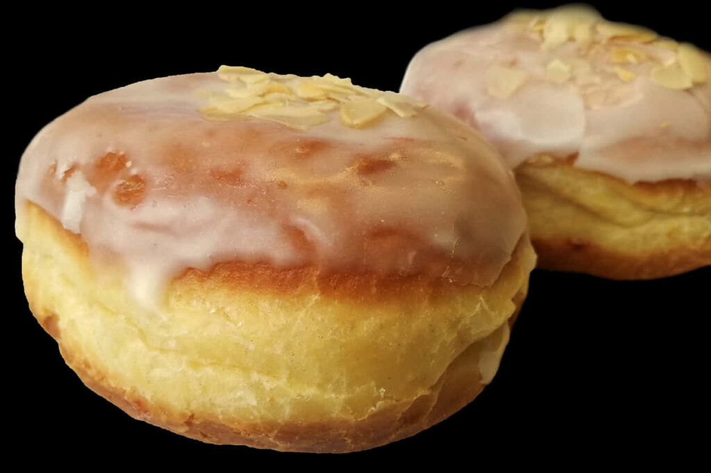 Glazed Almond Donuts Close-Up: Iced Delight on Black Wallpaper