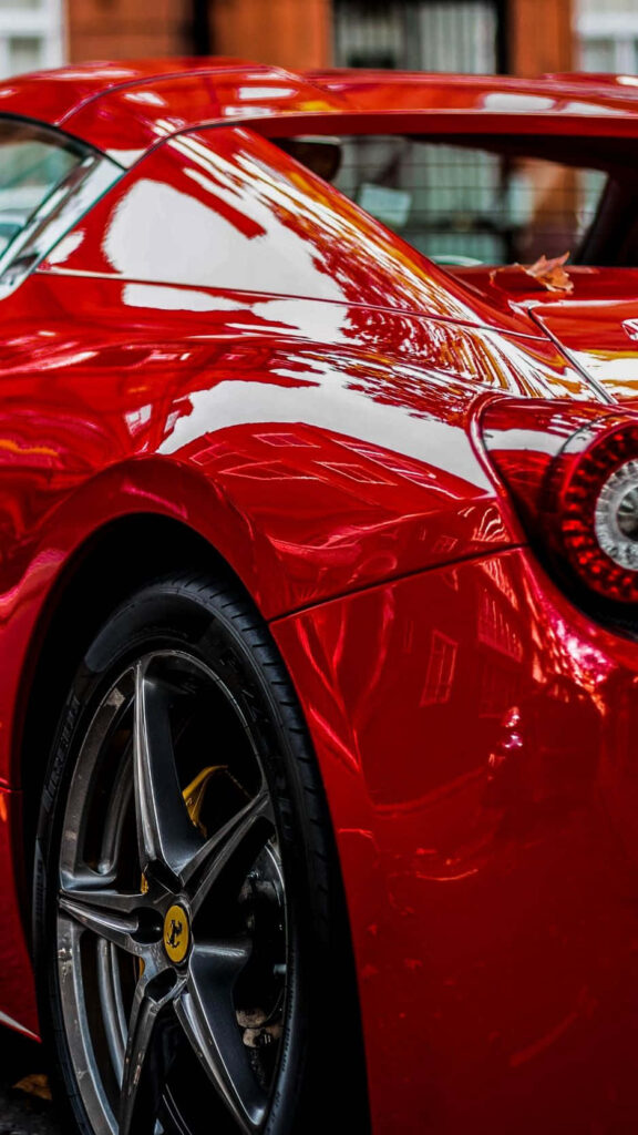 Sleek red Ferrari parked outdoors gleaming under natural light with polished curves wallpaper background