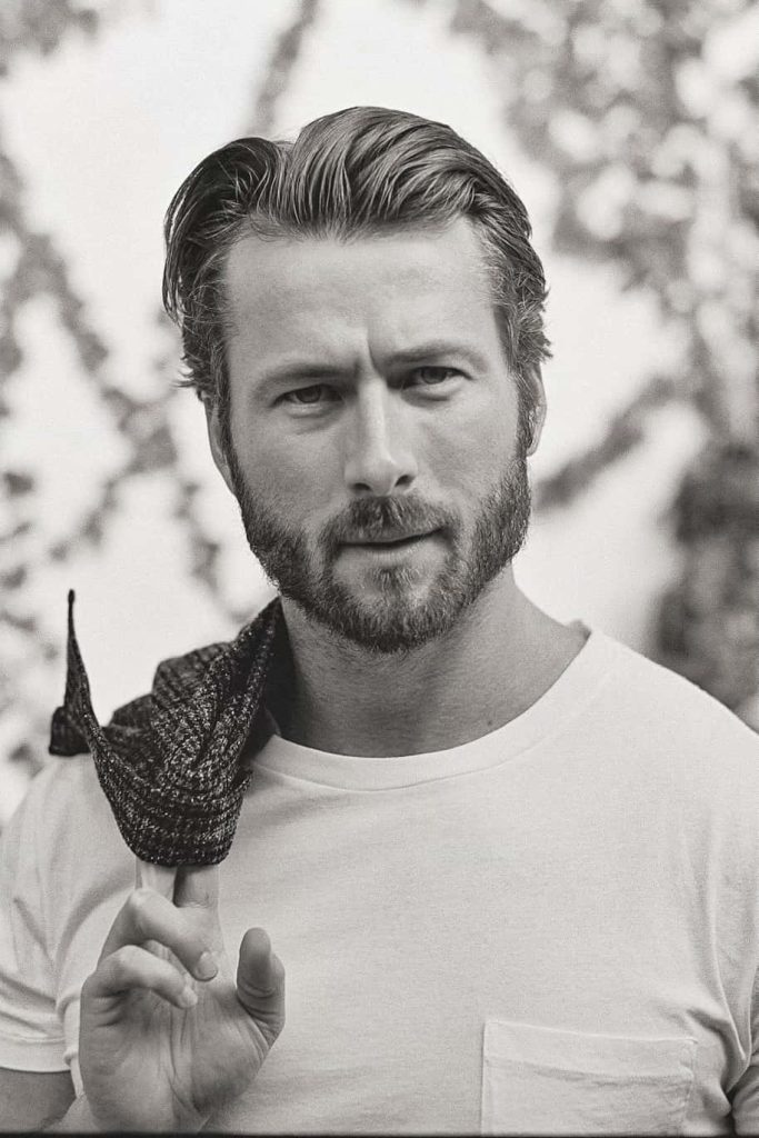 Monochrome portrait of actor Glen Powell wearing white t-shirt and textured jacket background Wallpaper