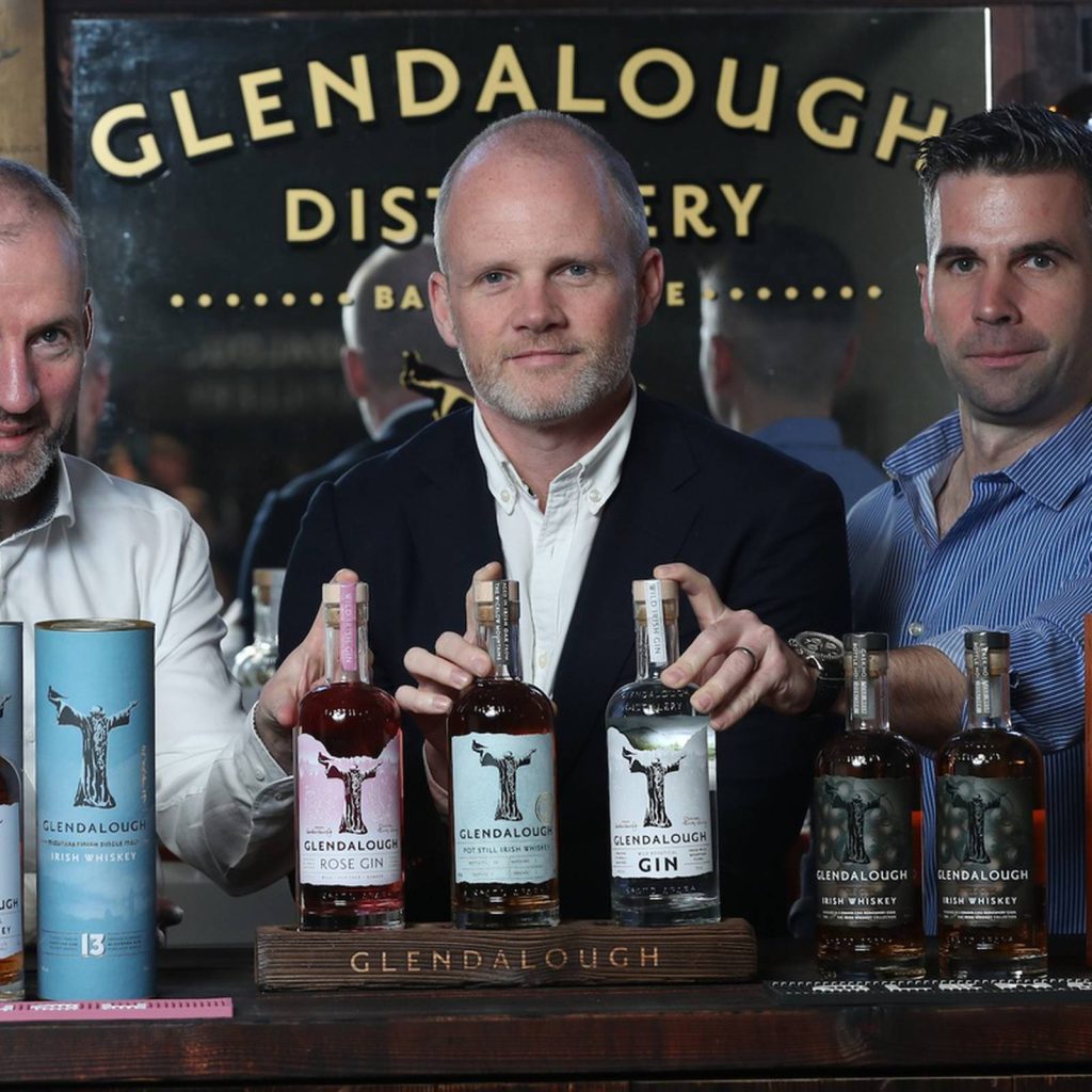 Glendalough Distillery team showcasing Rose Gin Pot Still Irish Whiskey and Dry Gin bottles Wallpaper