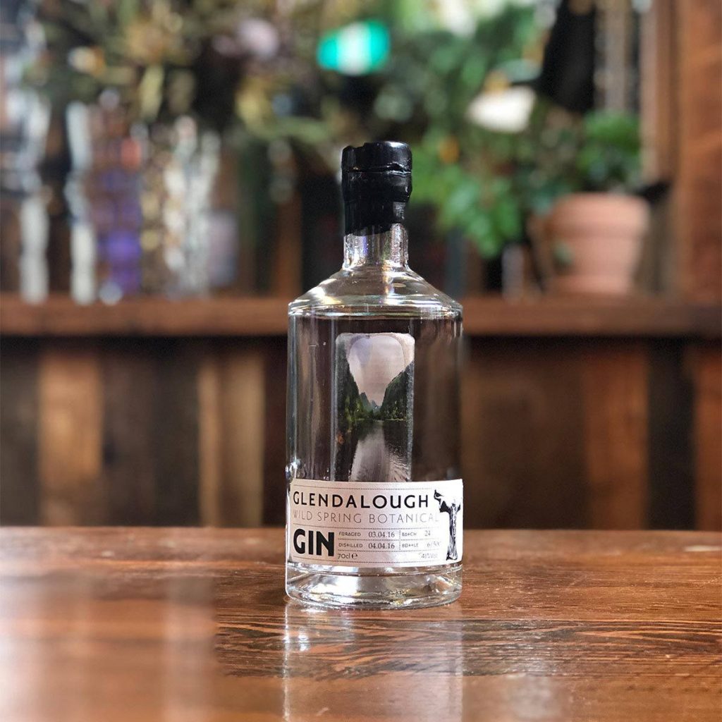 Glendalough Wild Spring Botanical Gin bottle on rustic wood bar top with warm blurred background Wallpaper