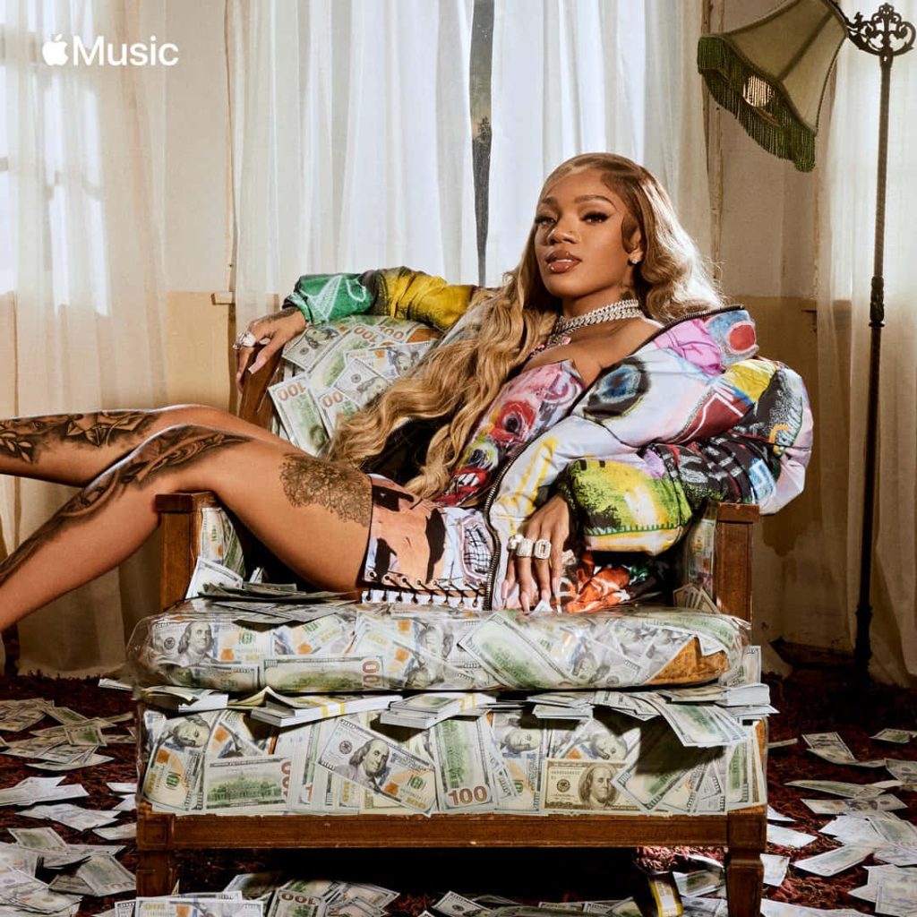 Rapper GloRilla in colorful jacket sits in armchair with stacks of hundred-dollar bills bold confident pose Wallpaper