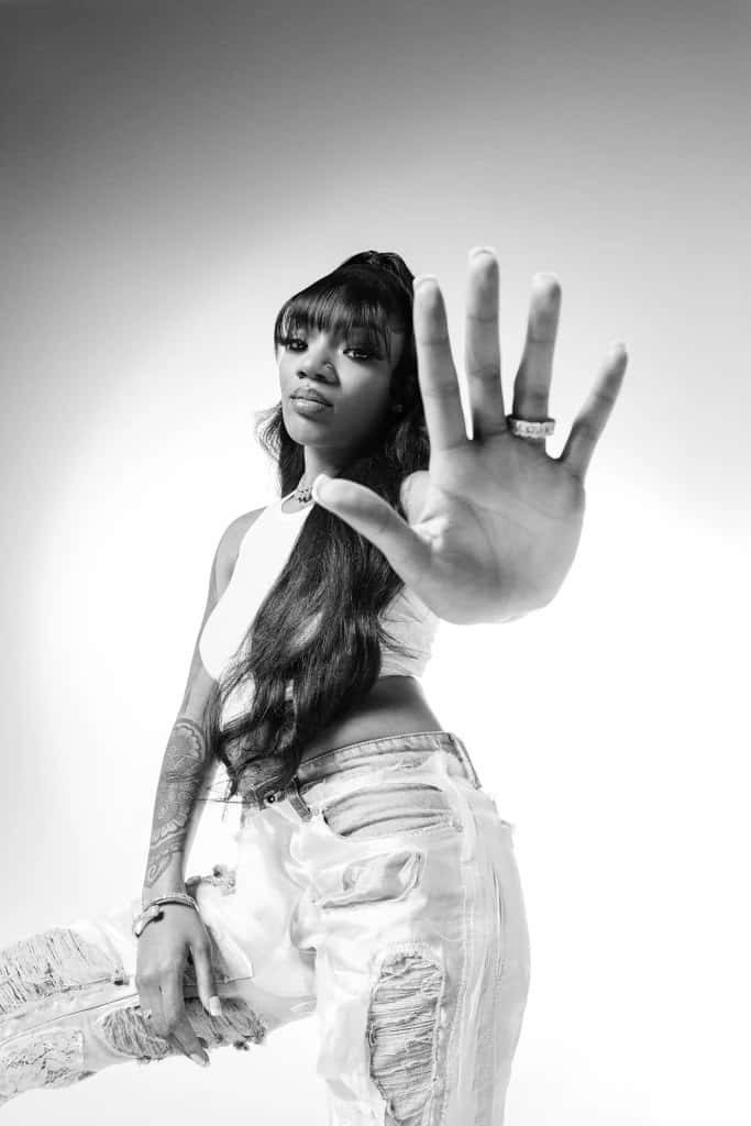 Black-and-white portrait of rapper GloRilla with long hair ripped denim and tattoos confident pose Wallpaper