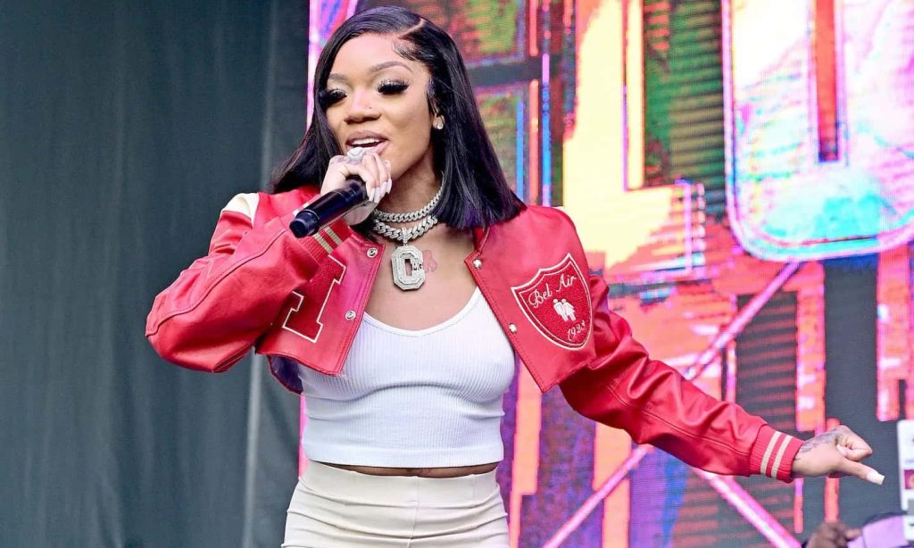 Rapper GloRilla performing live in red varsity jacket and iced chain on vibrant concert stage Wallpaper
