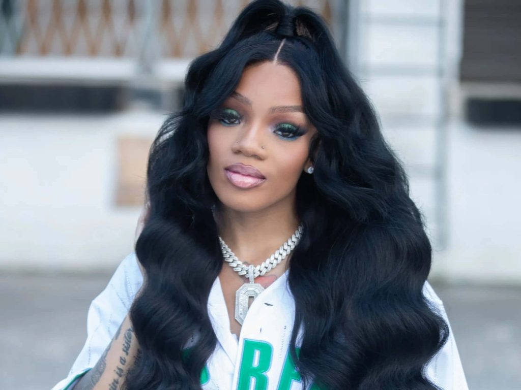 Rapper GloRilla portrait wallpaper with long wavy hair bold green eyeshadow white jersey iced chain