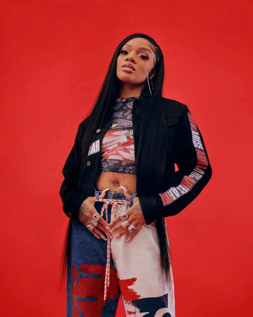 Portrait of rapper GloRilla in black jacket and two-tone pants on vibrant red background Wallpaper