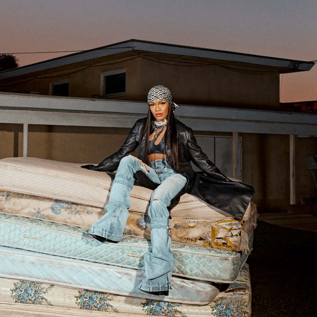 Rapper GloRilla poses on worn mattresses in leather jacket and headscarf at urban sunset wallpaper