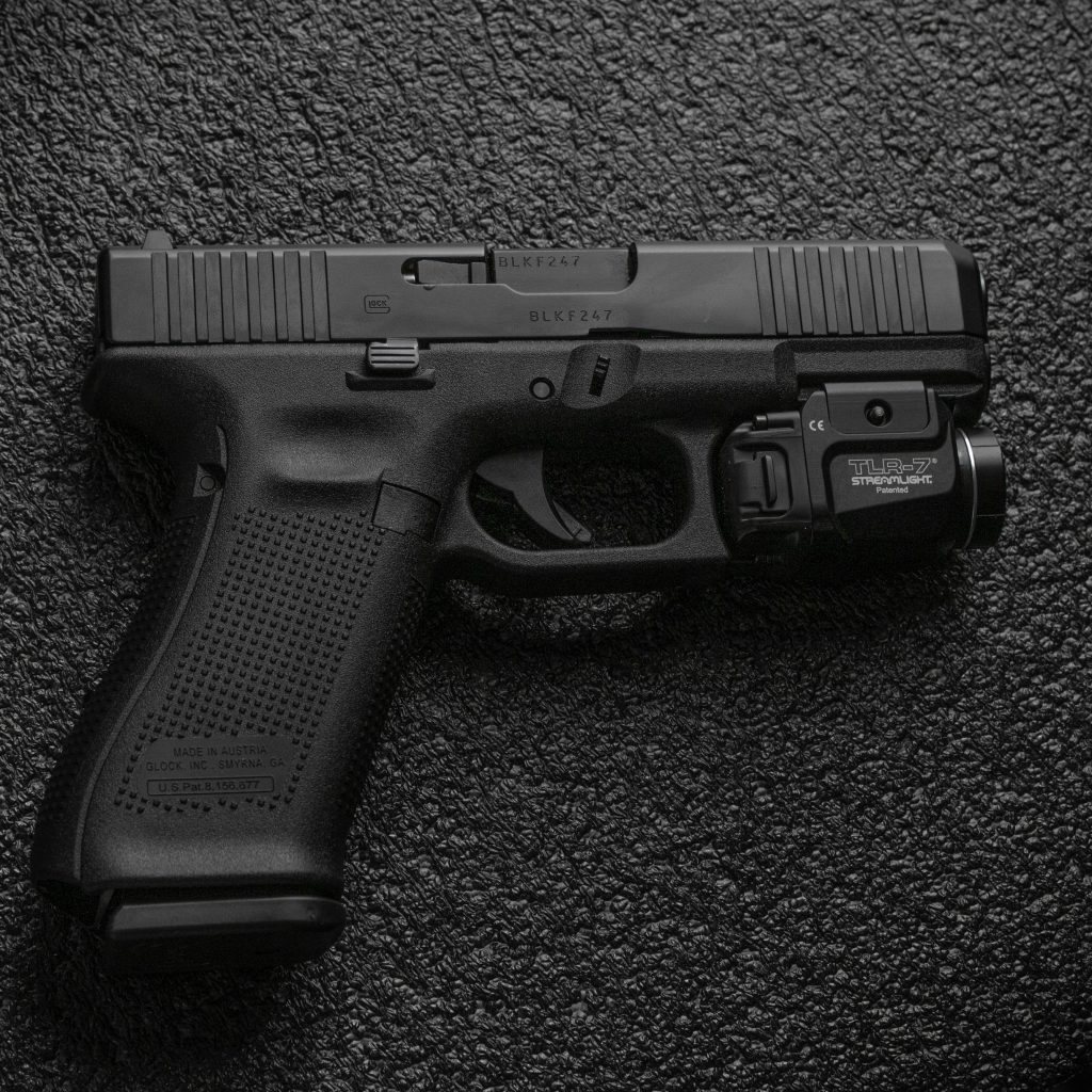 Glock pistol with Streamlight TLR-7 light on dark textured tactical background high-detail wallpaper