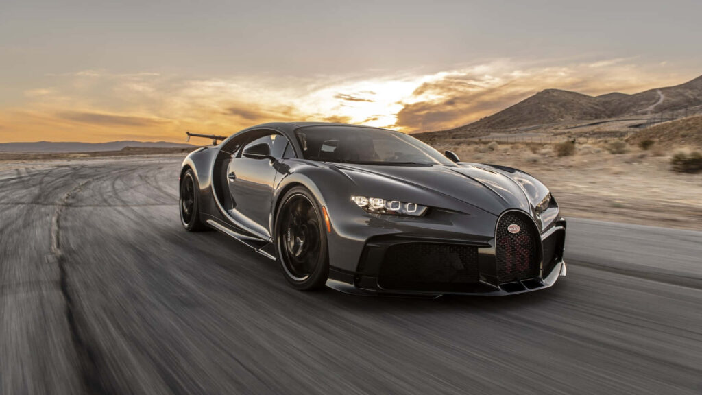 Glossy black Bugatti Chiron speeding on mountain road at sunset luxury high performance wallpaper