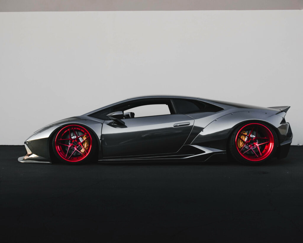 Glossy black Lamborghini Huracán with bold red rims side profile on minimal wallpaper background
