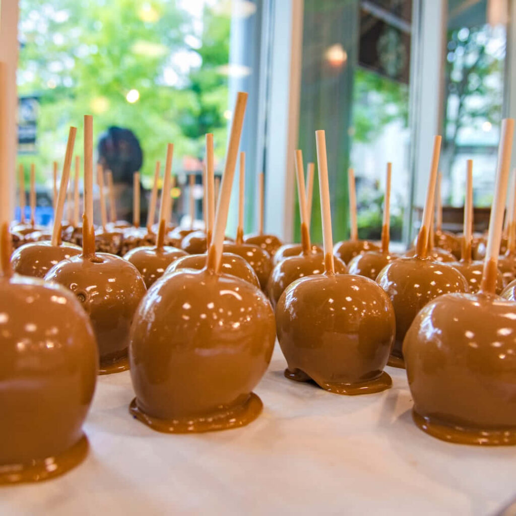 Glossy caramel apples rows with creamy coating in bright kitchen festive wallpaper background