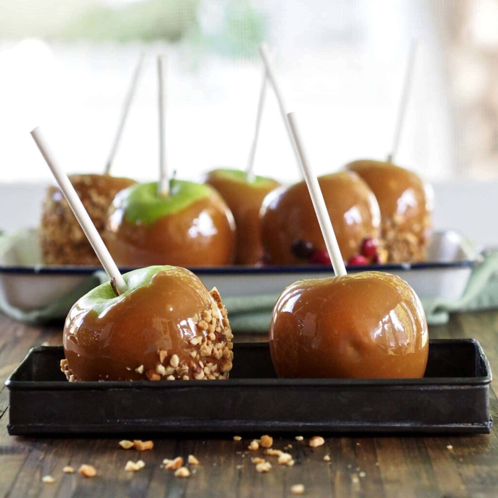 Glossy caramel apples on rustic trays with nuts and vibrant green apples autumn dessert wallpaper