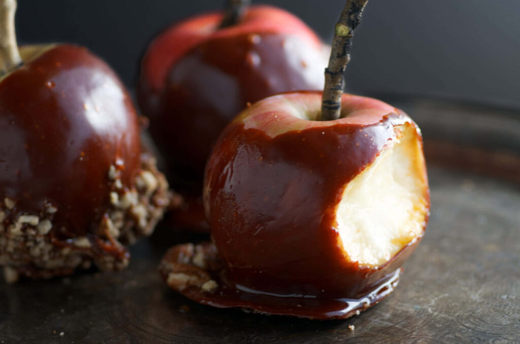 Glossy caramel apples on rustic wooden table close-up autumn festive wallpaper background