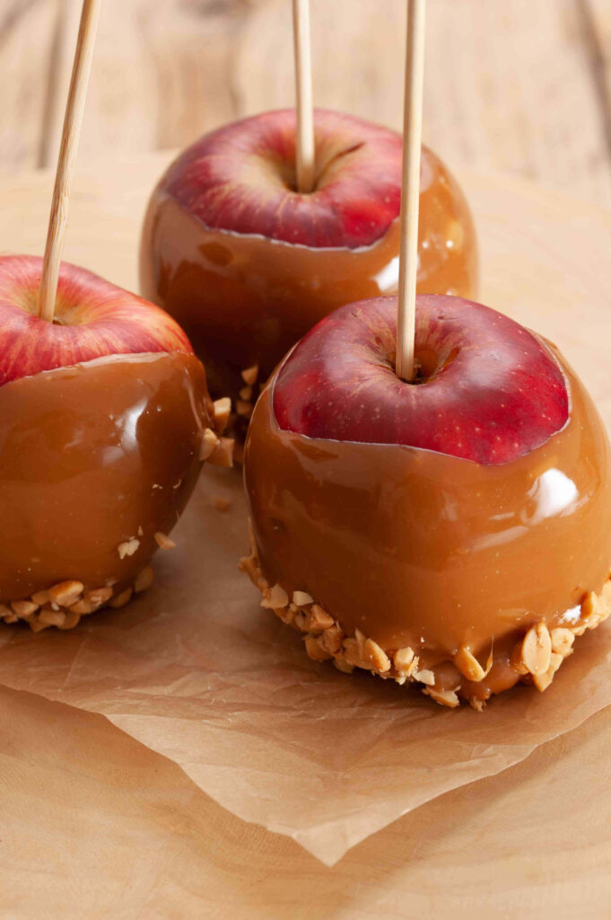 Glossy caramel apples with nut toppings on rustic table autumn wallpaper background close-up