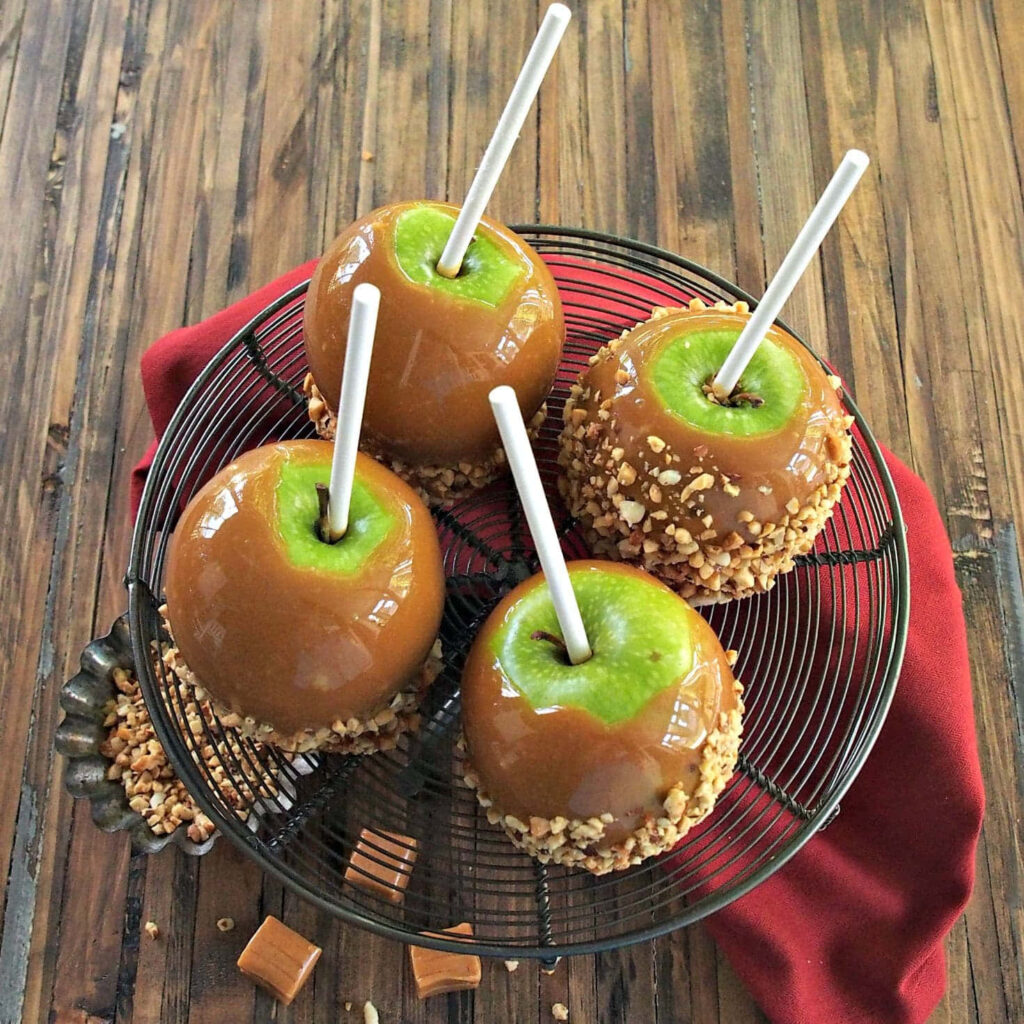 Glossy caramel apples with crushed nuts on wire rack over rustic wood autumn wallpaper background