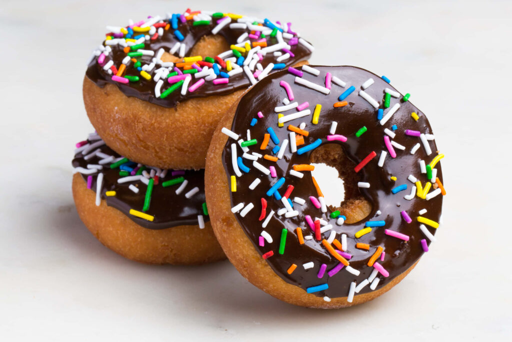 Stacked golden donuts with glossy chocolate icing and rainbow sprinkles on light background Wallpaper