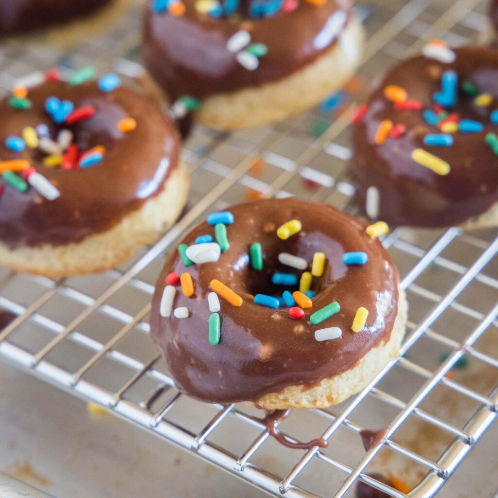 Freshly baked chocolate glazed donuts with rainbow sprinkles on metal cooling rack wallpaper
