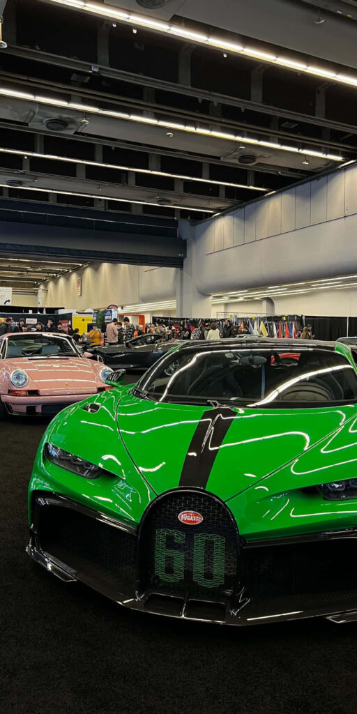 Glossy green Bugatti Chiron with black racing stripes displayed indoors at luxury auto show Wallpaper
