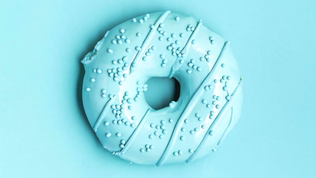 Minimalist pastel blue donut with white candy sprinkles on matching light blue background wallpaper